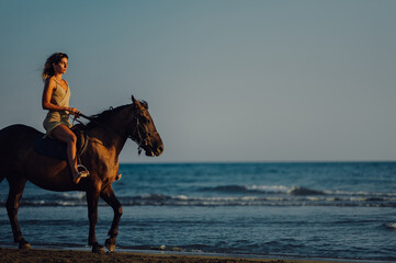 A seductive lady is horseback riding at the beach at sunset.