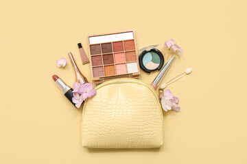 Cosmetic bag with makeup products for eyes, lipstick and flowers on light yellow background