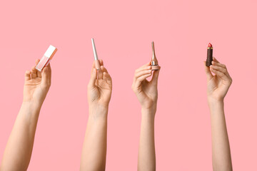 Female hands with lipstick, lip gloss and eyeliners on pink background