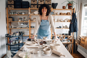 Portrait of young craftswoman standing at pottery studio and smiling.