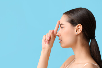 Young woman touching her nose on blue background. Plastic surgery concept