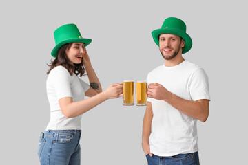 Happy young couple in leprechaun hats with glasses of beer on grey background. St. Patrick's Day...