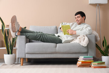 Young man reading book on sofa at home