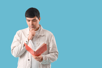 Thoughtful young man reading book on blue background