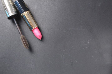 Make-up at home. Brown mascara and lipstick lie on a black background, top view. A place for a...
