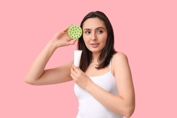 Beautiful young woman with hair scalp massager and cosmetic cream on pink background