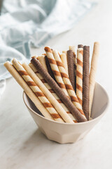 Assorted Chocolate and Vanilla Cream Filled Wafer rolls in bowl on white table.