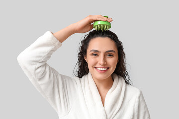 Plakaty  Beautiful young woman using hair scalp massager on grey background