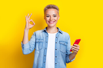 Photo portrait of lovely young lady hold telephone show okey symbol wear trendy jeans garment isolated on yellow color background