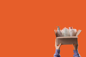Woman with cosmetic products in moving box on orange background