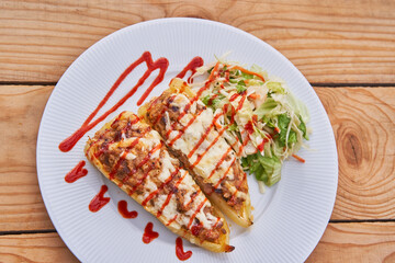 Yellow sweet paprika or peppers stuffed by minced pork meat and covered by sheep cheese and sprinkled by red chilli sauce on the white porcelain plate served with small lettuce salad as a side dish.