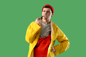 Thoughtful young sailor in raincoat with smoking pipe on green background