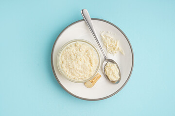 Horseradish sauce in plate with bowl, spoon and ground horseradish root on blue background. Top view