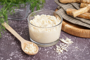Horseradish sauce in bowl and spoon with ground horseradish on grey background