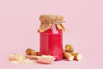 Horseradish sauce with beet in jar and spoon with ground horseradish on pink background