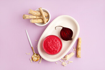 Horseradish sauce with beet in bowl and pieces of beet on lilac background. Top view