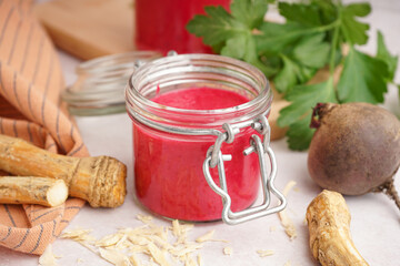 Horseradish sauce with beet in jar and horseradish root on white table
