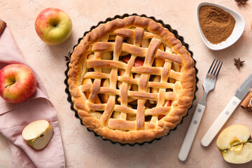 Tasty homemade apple pie with fruits, cinnamon and cutlery on beige grunge background