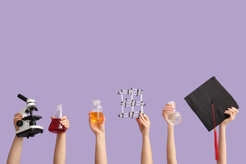 Female hands holding filled flasks with molecular model, microscope and graduation hat on lilac background. Chemistry lesson concept