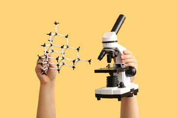 Female hands holding molecular model with microscope on yellow background. Chemistry lesson concept