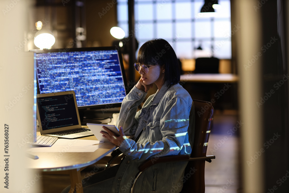 Poster female programmer working with tablet computer in office at night
