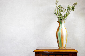 Modern summer still life photo. vase with green olive tree branch on wood table near gray wall...