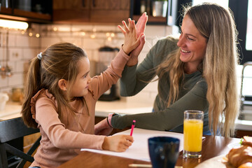 Morning joy in the kitchen: A smiling mother teaches her preschooler the art of writing letters at...