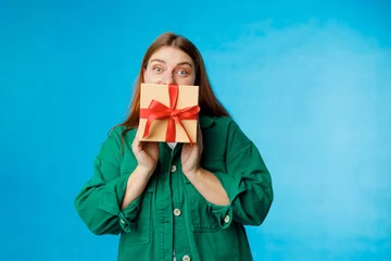 Fotobehang Portrait of cheerful, happy 30s woman holding wrapped present, celebrating birthday on blue background. Valentine's Day Women's Day birthday holiday concept. © mdyn