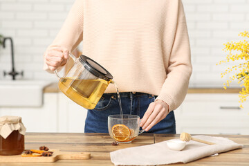 Young woman pouring green tea from teapot into cup in kitchen