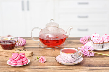 Teapot and cup of hibiscus tea with sweets on table in kitchen