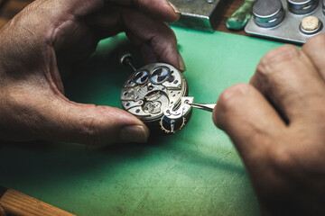 A watchmaker's hands remove a part of a watch mechanism with tweezers.