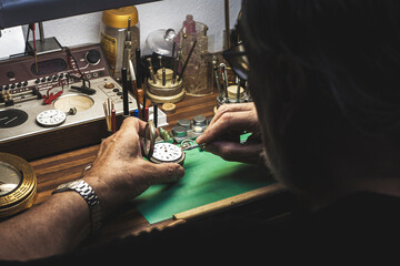 Watchmaker repairing a clock mechanism at his workbench full of different specialised tools.