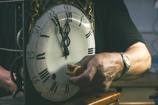 The hands of a watchmaker winding the hands of a wall clock.