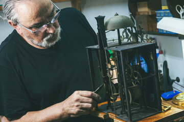 Clockmaker making adjustments to the gears of a large wall clock.