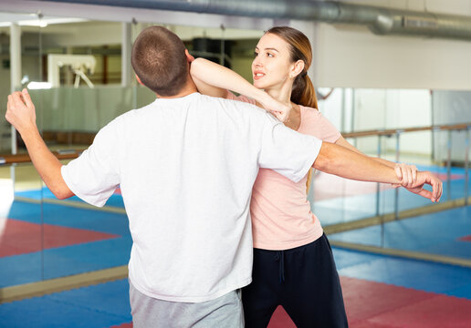 Focused girl performing elbow strike and wristlock, painful control move to immobilize male opponent during self defence training in gym