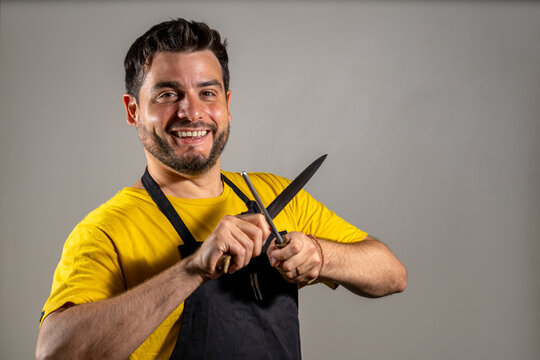 Carnicero afilando su cuchillo mientras sonr&iacute;e a c&aacute;mara. Fotograf&iacute;a con  Copy Space