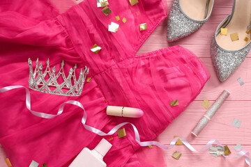 Prom dress with crown, high heel shoes and makeup products on pink wooden background