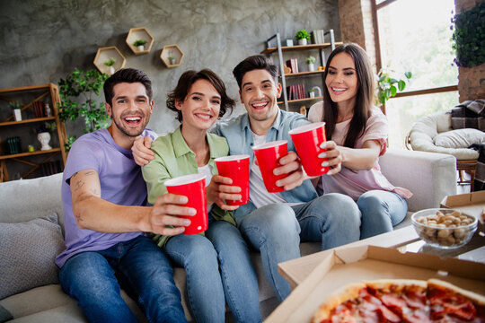 Photo of group funky best friends sit comfort couch hug clink plastic beer cups loft apartment indoors