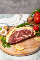 Buttered ribeye. Raw ribeye surrounded by butter on wood serving board. Close up