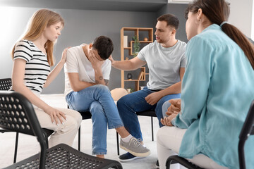 Young people calming sad man at group therapy session
