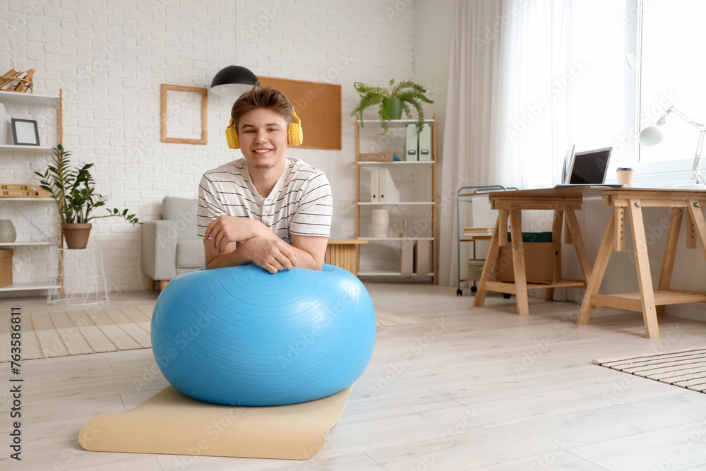 Canvas Prints Young man in headphones on fitball at home