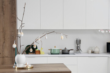 Vase with tree branches and Easter eggs on dining table in light kitchen