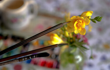 Artistic brushes close up on blurred background of watercolor pallet and flowers