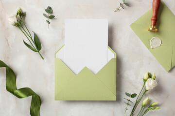 Olive color envelope with blank paper card inside and wedding stationery with flowers on stone background.