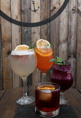 Cocktails with a rustic wooden background. Closeup view of four glasses with drinks, a vodka and orange juice screwdriver, a red berries daiquiri, a negroni and a grapefruit gin tonic. 