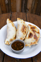 Finger food. Closeup view of three meat empanadas with chimichurri spicy sauce in a white bowl on the wooden table.	
