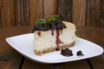 Desserts. Closeup view of a slice of Cheesecake with mascarpone cheese and berries dressing, in a white dish on the wooden table.	