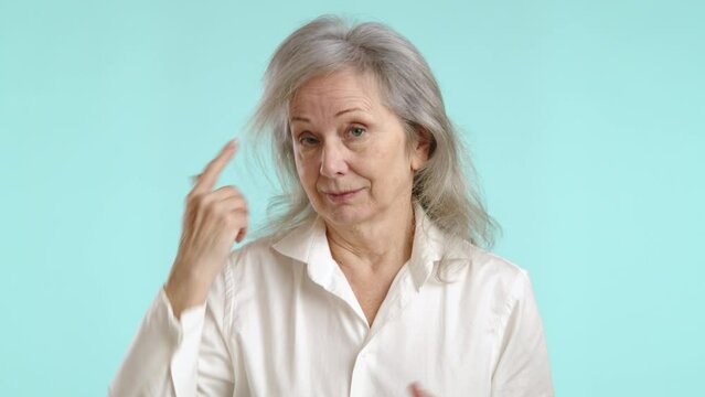 Mature woman pointing to her head with a finger, making the universal gesture that suggests she thinks someone might be out of their mind. Camera 8K RAW. 