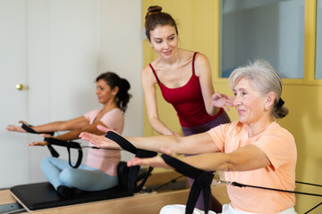 Fototapeta na wymiar Portrait of a mature woman practicing Pilates in group training with a female instructor, doing exercise on a simulator, ..sitting in the lotus position