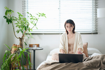 ベッドでノートパソコンを使う20代女性 - obrazy, fototapety, plakaty